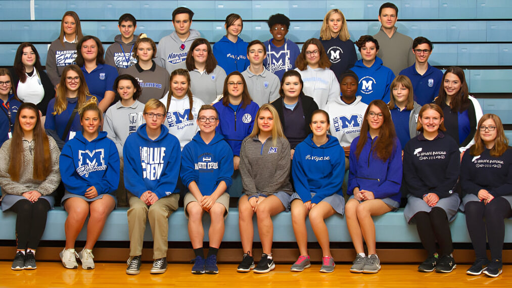 Eine Gruppe von Schülerinnen und Schülern in blauen und weißen Schuluniformen posiert in der Turnhalle der Marquette High School.