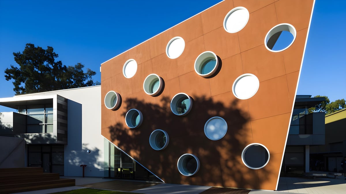 Das orangefarbene Gebäude der Marryatville High School mit runden Fenstern und Baum-Schatten an der Fassade ist vor blauem Himmel zu sehen.