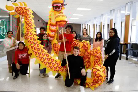 Eine Gruppe Schüler in traditioneller chinesischer Kleidung mit einem großen Drachentanzkostüm im Flur der Martin Luther High School.