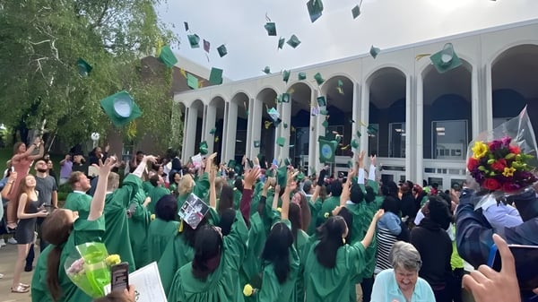 Eine Gruppe von Menschen in grüner Kleidung versammelt sich vor dem Gebäude der Martin Luther High School mit Bögen und Säulen.