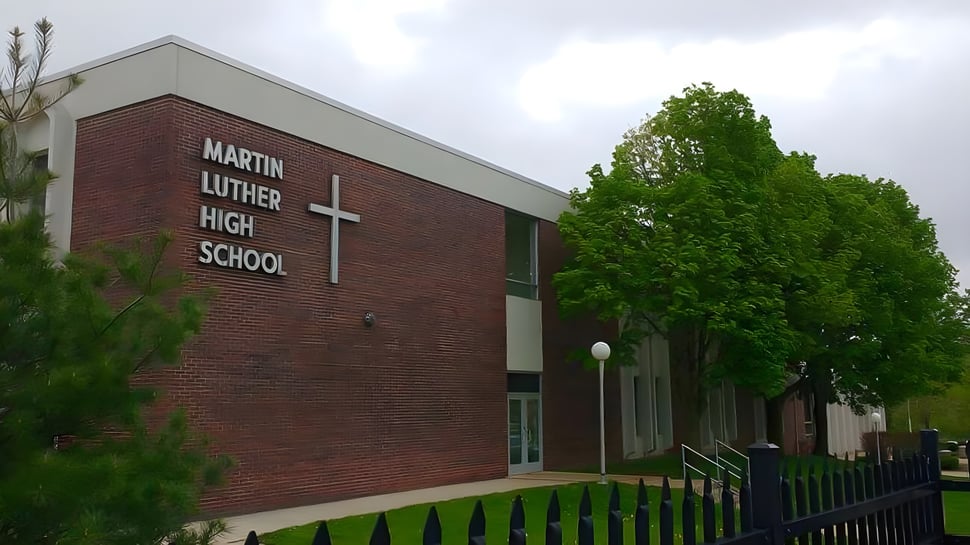 Das Backsteingebäude der Martin Luther High School ist von grünen Bäumen umgeben.
