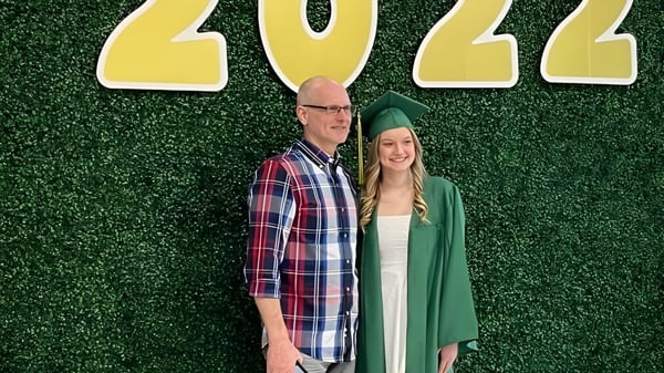 Zwei Absolventen der Martin Luther High School stehen vor einer grünen Hecke mit der Jahreszahl 2022.