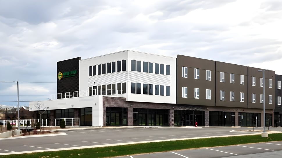 Das moderne Gebäude der Martin Luther High School mit Glas- und Backsteinfassade steht auf einem gepflasterten Parkplatz unter bewölktem Himmel.