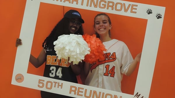 Zwei Personen posieren vor einer orangen Kulisse mit Text zum 50-jährigen Jubiläum am Martingrove Collegiate Institute.