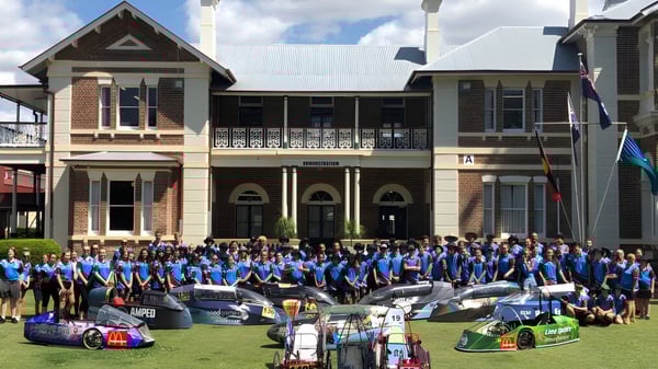 Schüler der Maryborough State High School versammeln sich vor einem historischen Gebäude neben mehreren Rennwagen.