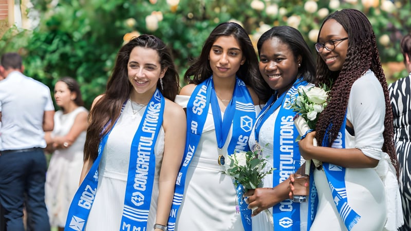 Schülerinnen der Marymount Academy International stehen draußen in einem grünen Garten und lächeln gemeinsam.