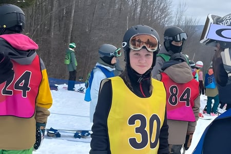 Eine Gruppe von Schülerinnen und Schülern der Marymount Academy trägt bunte Skikleidung und Helme und steht auf einem verschneiten Hang mit Bäumen.