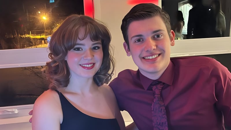 Zwei lächelnde Schülerinnen und Schüler der Marymount Academy posieren zusammen in einem Restaurant mit Blick auf die nächtliche Stadt.