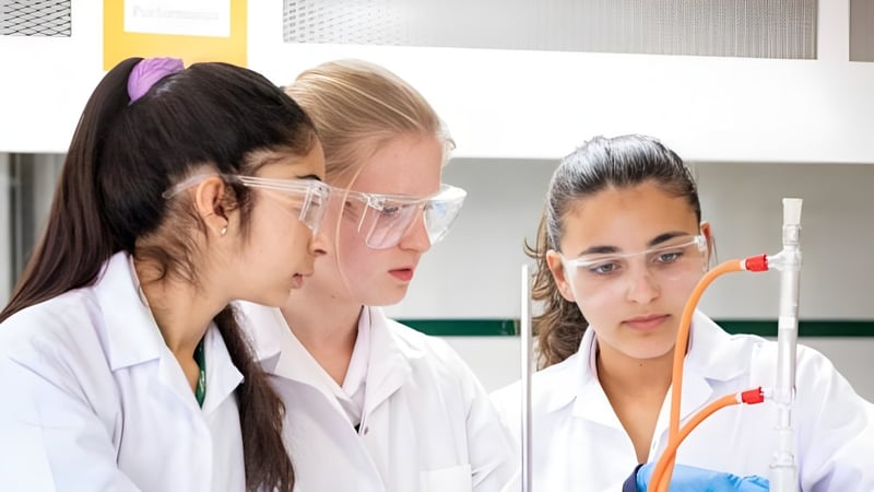 Drei Schülerinnen der Marymount International School untersuchen im Labor eine Probe in einem Reagenzglas.