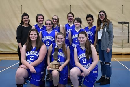 Eine Gruppe von Schülerinnen der Massey-Vanier High School posiert gemeinsam in blauen Basketballtrikots auf dem Spielfeld.