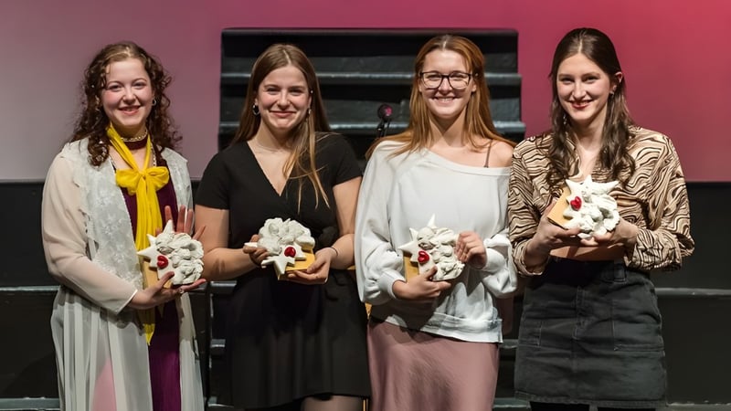Vier Schülerinnen der Massey-Vanier High School stehen mit weißen Blumensträußen vor einem pink-schwarzen Hintergrund.