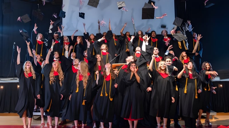 Eine Gruppe von Schülerinnen und Schülern der Master's Academy and College steht in schwarzen Talaren und roten Schärpen gemeinsam auf einer Bühne bei der Abschlussfeier.