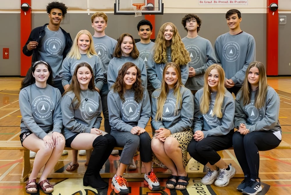Schüler der Master's Academy and College sitzen gemeinsam in der Turnhalle und posieren für ein Teamfoto in grauen Schuluniformen.