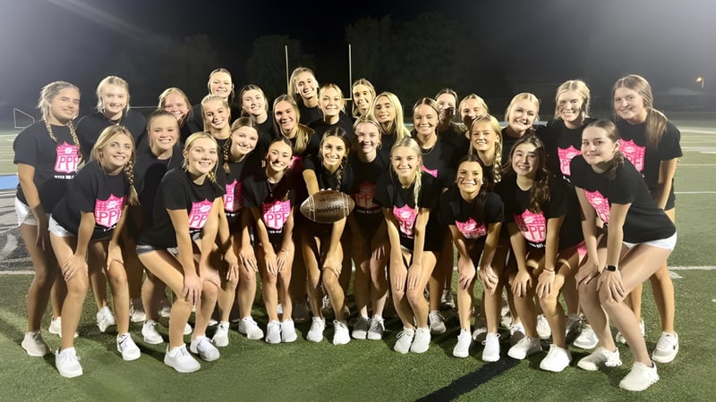 Cheerleader der Mater Dei Catholic High School posieren in einheitlichen Uniformen auf dem Sportfeld bei Nacht unter hellen Lichtern.