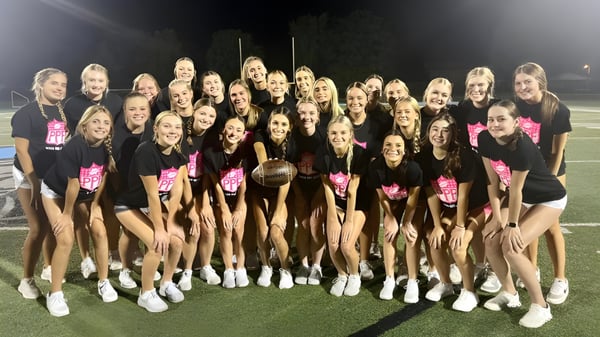 Cheerleader der Mater Dei Catholic High School posieren in einheitlichen Uniformen auf dem Sportfeld bei Nacht unter hellen Lichtern.