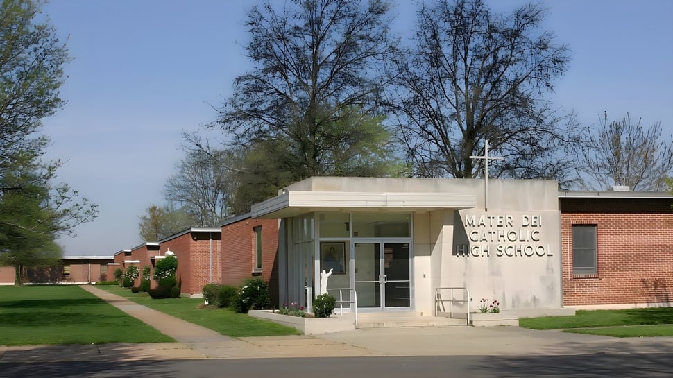 Das moderne Backsteingebäude der Mater Dei Catholic High School steht auf einer Grünfläche mit Bäumen unter klarem Himmel.