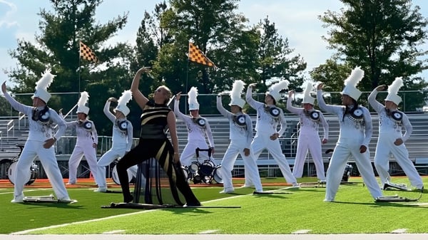 Eine Gruppe von Darstellern in weißen und schwarzem Outfit steht auf einer Wiese auf dem Gelände der Mater Dei Catholic High School.