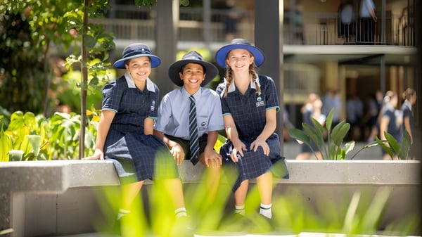 Drei Schülerinnen und Schüler des Matthew Flinders Anglican College stehen zusammen vor grüner Pflanzenkulisse und lächeln.