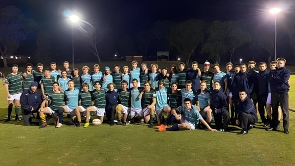 Eine große Gruppe von Schülerinnen und Schülern des Matthew Flinders Anglican College posiert gemeinsam auf einem beleuchteten Sportfeld bei Nacht.