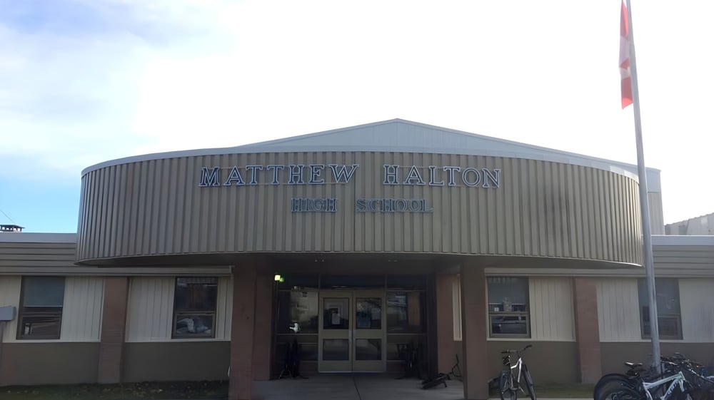 Das graue kuppelförmige Gebäude der Matthew Halton High School mit dem Schriftzug am Haupteingang und einem Fahrrad davor.