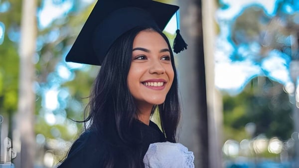 Eine junge Frau in Abschlusskleidung steht vor natürlichem Hintergrund auf dem Gelände der Matthew Halton High School.