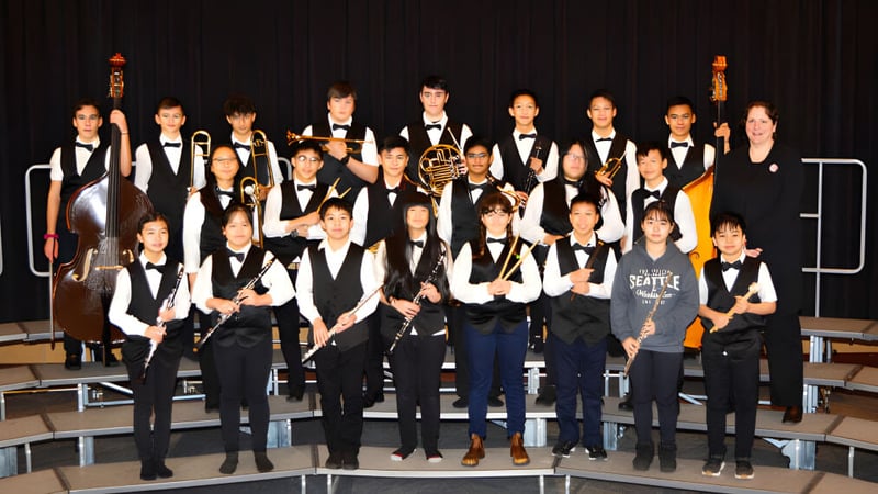 Eine Gruppe von Schülerinnen und Schülern der Matthew McNair Secondary School steht in formeller Kleidung auf einer Bühne vor dunklem Hintergrund.