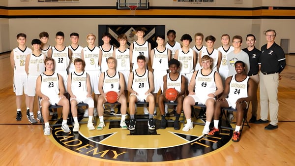 Das Basketballteam der Maur Hill-Mount Academy posiert gemeinsam mit den Trainern auf dem Spielfeld vor dem Mannschaftslogo.