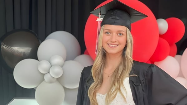 Eine Schülerin der Maxwell Heights Secondary School steht in ihrem Abschlussmantel vor roten und weißen Luftballons.