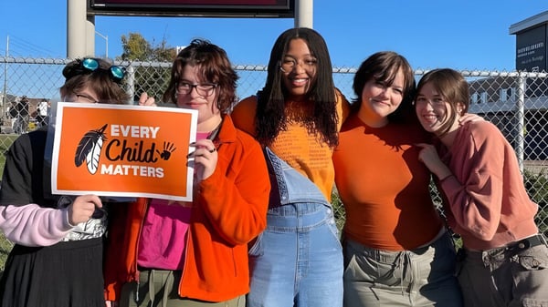 Eine Gruppe junger Mädchen mit einem Schild 'Every Child Matters' steht vor einem Zaun auf dem Gelände der Maxwell Heights Secondary School.
