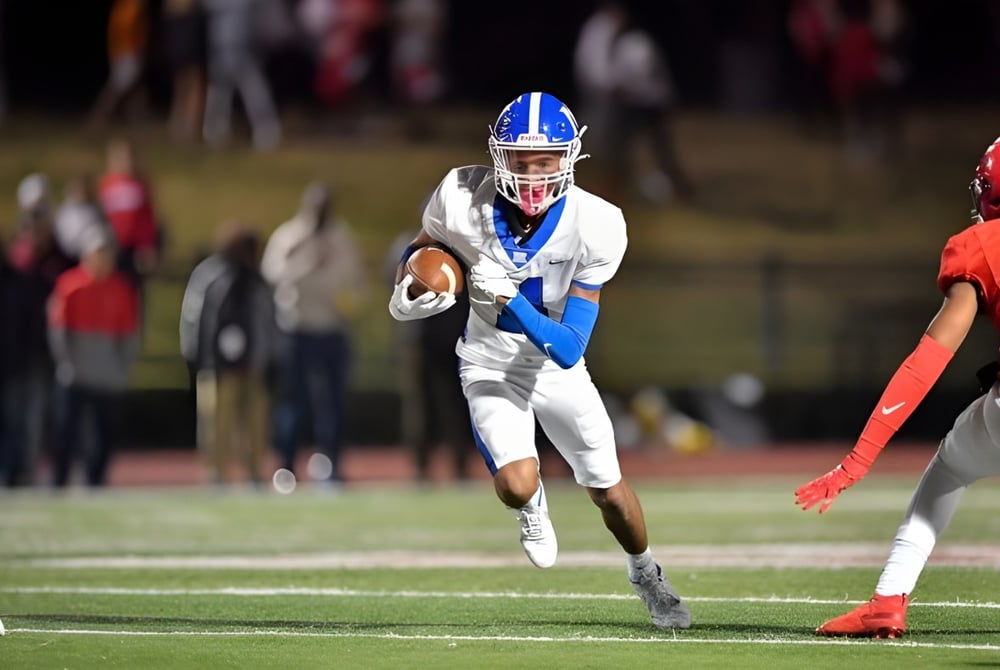 Ein Footballspieler in weißer Uniform mit blauen Akzenten läuft mit dem Ball auf dem Footballfeld der McCallie School.