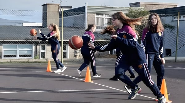 Schülerinnen des McEgan College spielen Fußball auf einem Freiluft-Sportplatz mit Gebäuden im Hintergrund.