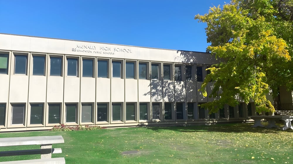 Das moderne mehrstöckige Gebäude der McNally High School ist von grüner Vegetation umgeben unter blauem Himmel.