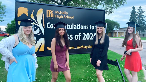 Vier Schülerinnen posieren vor einem Schild mit Glückwünschen für die Abschlussklasse 2022 der McNally High School.