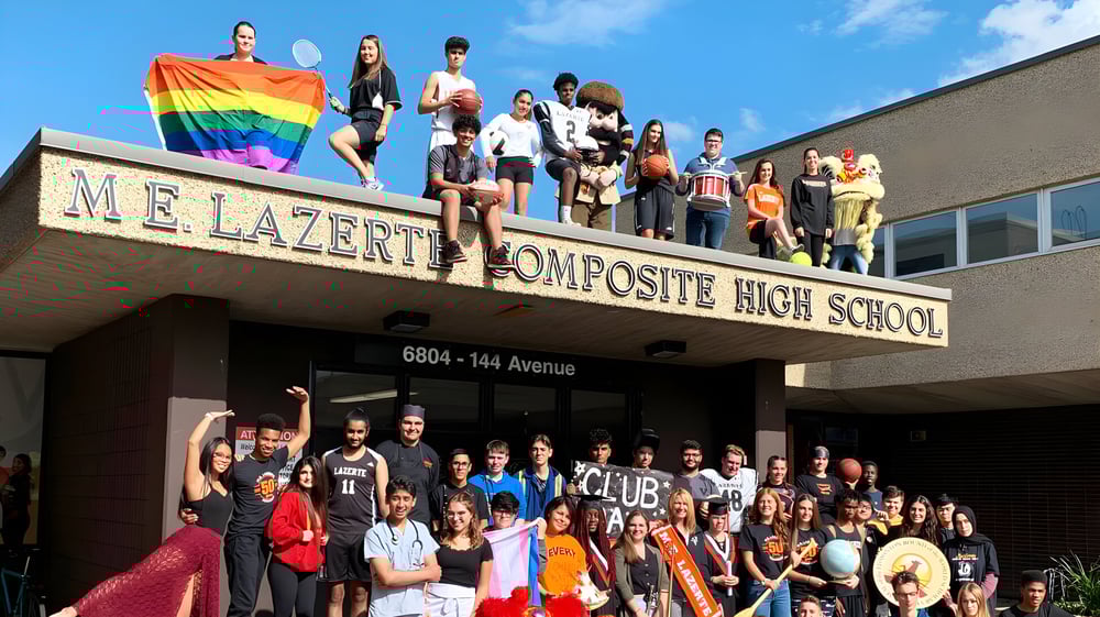 Schüler und Mitarbeiter der M.E. LaZerte Composite High School stehen vor dem Schulgebäude mit einer deutlichen Regenbogenflagge.