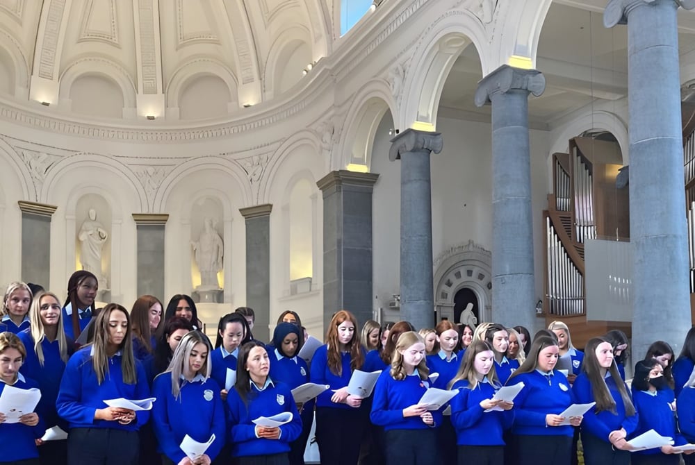 Eine Gruppe von Schülern der Meán Scoil Mhuire Longford steht in blauen Roben in der großen, kunstvoll gestalteten Kathedrale.