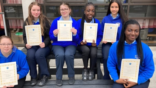 Schüler der Meán Scoil Mhuire in Longford stehen in blauen Uniformen mit Urkunden vor einem Backsteingebäude.