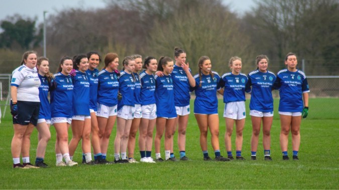 Eine Gruppe junger Fußballspielerinnen in blauen Trikots steht auf einem Spielfeld auf dem Campus der Meán-Scoil Mhuire Gan Smál.