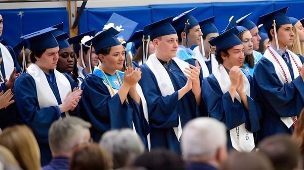 Eine Gruppe von Absolventen der Medway High School steht in blauen Talaren vor einem blauen Hintergrund und blickt zur Kamera.