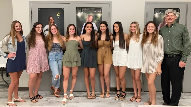 Eine Gruppe Schülerinnen steht vor einem Gebäude auf dem Campus der Melbourne Central Catholic High School mit einem Mann im Hintergrund.