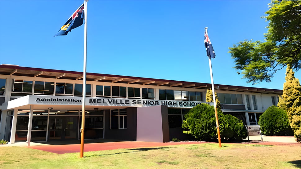 Der Haupteingang der Melville Senior High School mit australischer und Western Australian Flagge im Vordergrund und Bäumen im Hintergrund.