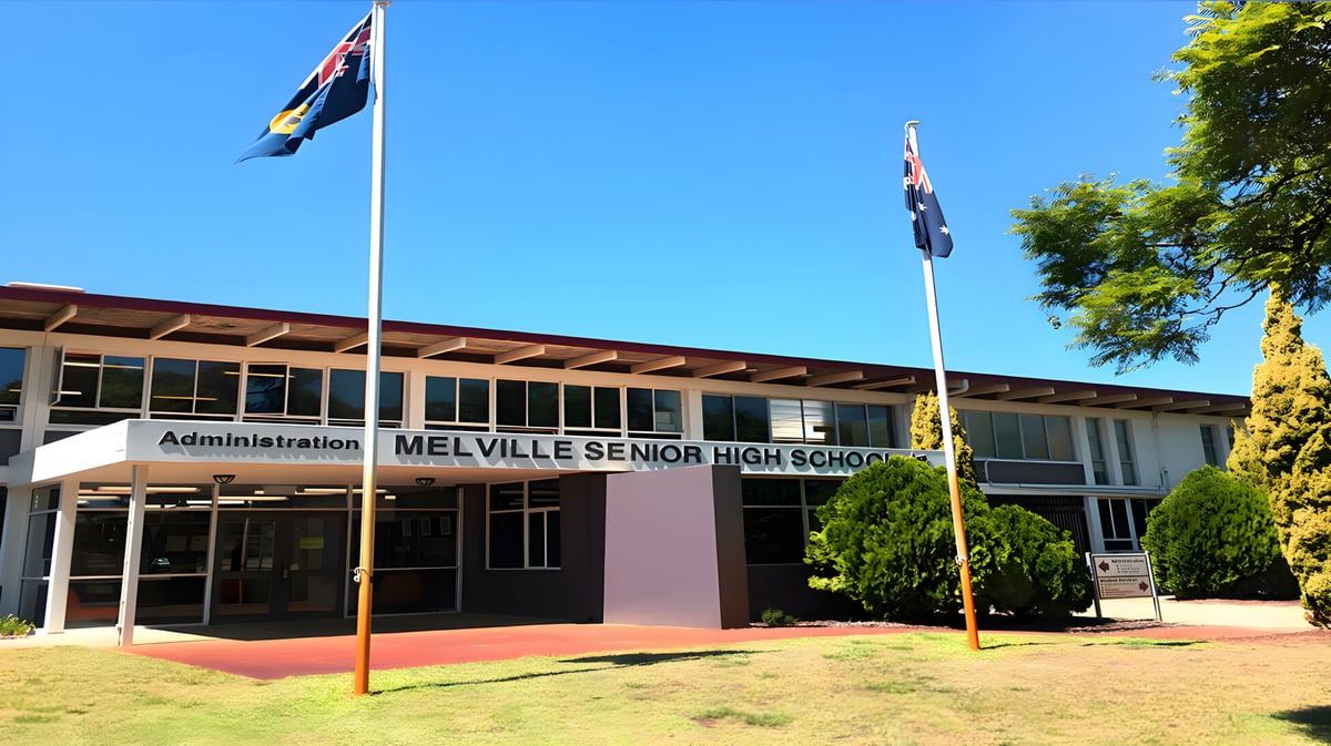 Der Haupteingang der Melville Senior High School mit australischer und Western Australian Flagge im Vordergrund und Bäumen im Hintergrund.