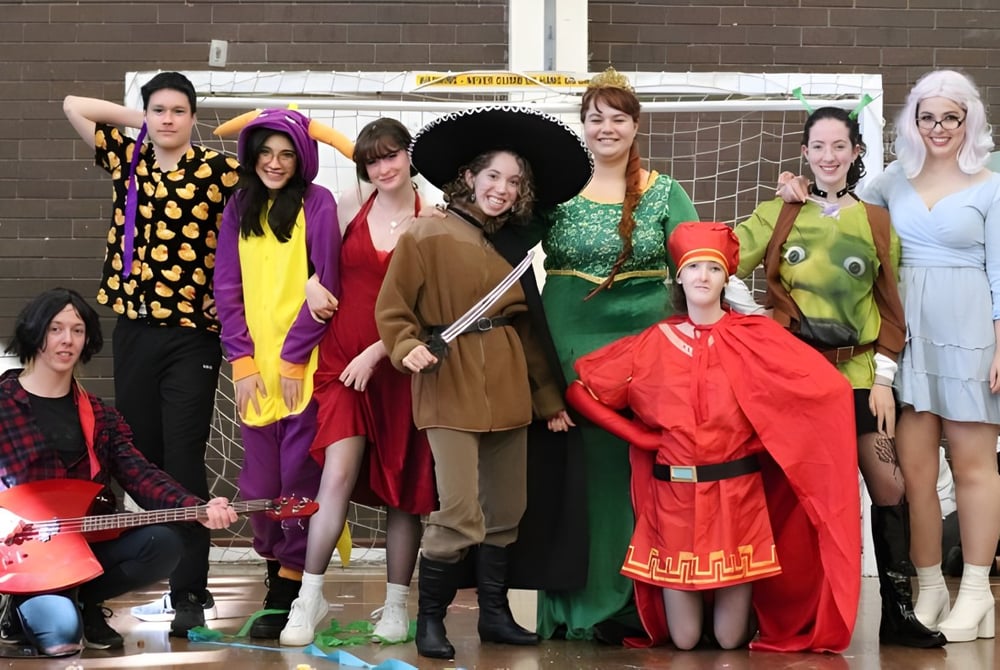 Eine Gruppe Schüler der Melville Senior High School posiert in bunten, lebendigen Kostümen vor einer Backsteinwand.