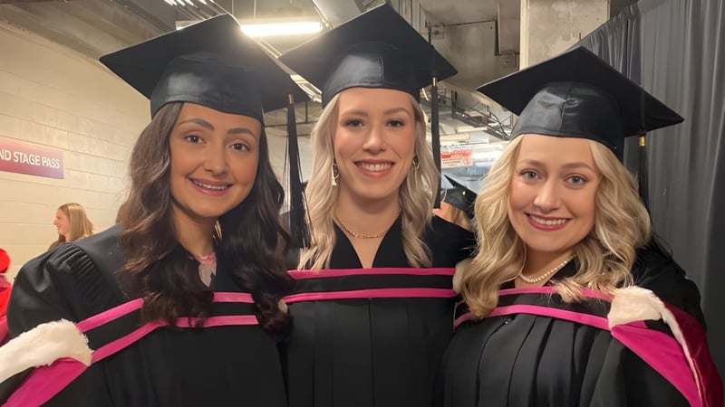 Drei Absolventinnen der Memorial University posieren in ihren Talaren und Mützen in einem Flur.