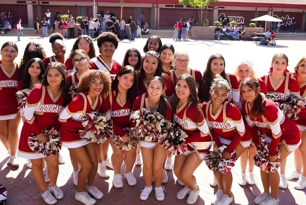 Eine Gruppe Cheerleader in roten Uniformen posiert mit Pompons im Freien auf dem Gelände des Merced Union High School District.