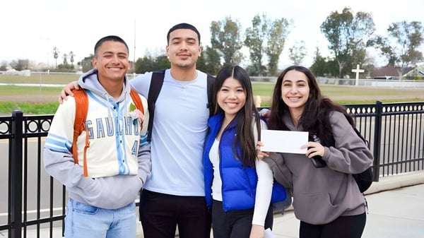 Vier Schülerinnen und Schüler des Merced Union High School District stehen draußen in einem parkähnlichen Bereich mit Bäumen und Geländer.