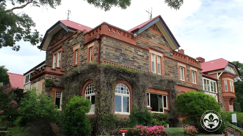 Das auffällige Backsteingebäude mit rotem Ziegeldach auf dem Campus des Mercedes College wird von Bäumen umgeben.