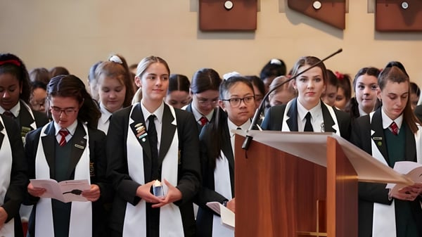Schüler des Mercedes College stehen in formeller Kleidung im Raum mit Holzvertäfelung am Podium.