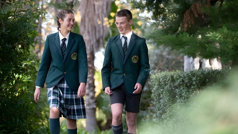 Zwei Schüler in Schuluniformen gehen zusammen auf einem Weg umgeben von üppigem Grün auf dem Campus des Mercedes College.