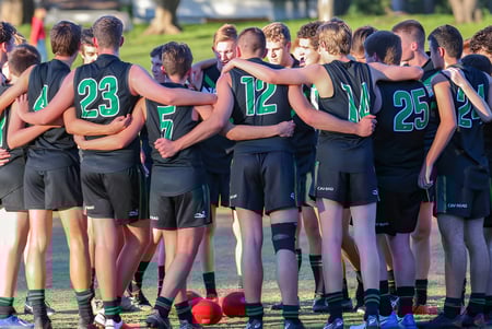 Eine Gruppe junger Athleten des Mercedes College steht in einem Huddle auf einem Rasenfeld.