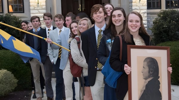 Eine Gruppe von Schülerinnen und Schülern der Mercersburg Academy steht vor einem Gebäude und hält ein gerahmtes Porträt.